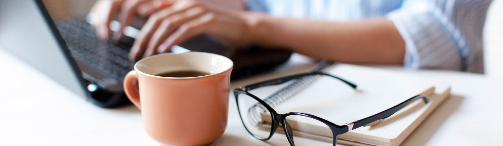 Coffee cup, glasses, and laptop on desk